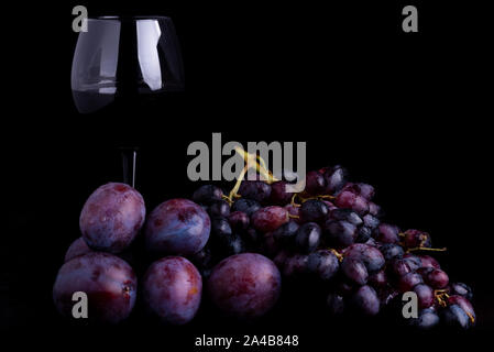 fresh blue plums, grapes and glass of wine on a black reflective background Stock Photo