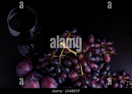 fresh blue plums, grapes and glass of wine on a black reflective background Stock Photo
