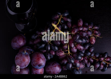 fresh blue plums, grapes and glass of wine on a black reflective background Stock Photo