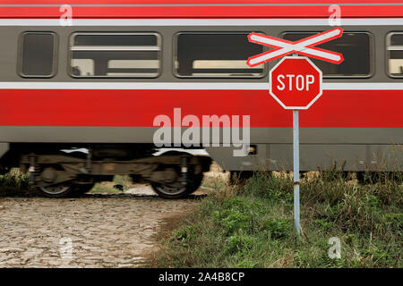 St Andrew's Cross and stop sign at railroad level crossing and country cobblestone road junction with train on rails Stock Photo