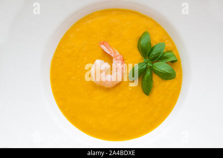 Tasty pumpkin cream soup with shrimps and fresh basil leaves, blended with spice and onion. Top view, close-up. Stock Photo