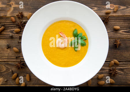 Tasty pumpkin cream soup with shrimps and basil leaves, blended with spice and carrots. Top view. Stock Photo