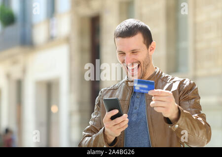 Excited man paying on line with credit card and mobile phone in the street Stock Photo