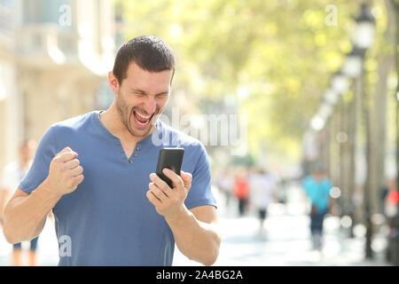 Excited man checking good news on mobile phone celebrating success in the street Stock Photo
