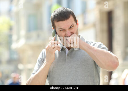 Angry man talking on mobile phone having problems standing in the street Stock Photo