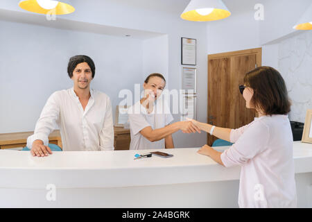 Guest checking in to hotel, male and female receptionists standing at the front desk talking and greeting woman guest Stock Photo