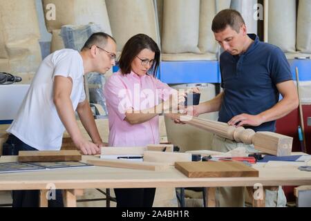 Group of industrial people client, designer or engineer and workers working together on project of wooden furniture. Teamwork in carpentry workshop. Stock Photo