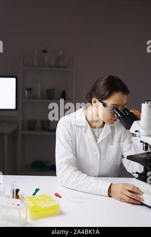 Portrait of young female scientist looking in microscope while doing research in medical laboratory, copy space Stock Photo
