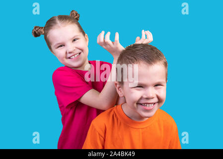 Little girl puts horns to a boy isolated on a blue background Stock Photo