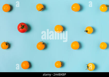 One red tomato cherry stand out from yellow tomatoes cherry. individuality and difference concept. flat lay Stock Photo