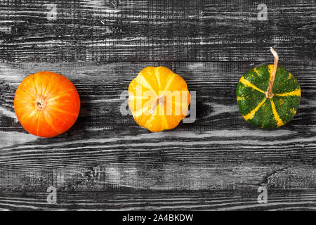Autumn minimalistic composition with orange, yellow and green pumpkins on dark wooden background. top view. flat lay Stock Photo