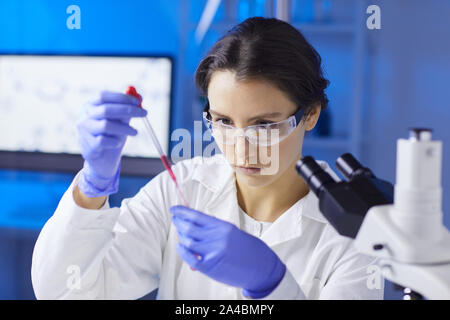 Portrait of young female scientist preparing blood test sample using dropper while working in medical laboratory, copy space Stock Photo
