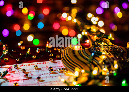 Guitar Music for the holiday season.  Jingle Bells sheet music, Christmas lights and small bells accompany a beautiful laminated wood electric guitar. Stock Photo
