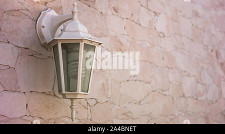 Hanging lamp on the side of a facade of a house and its garden, in a classic style, with glass and metal, and inside it spiral halogen bulb, the whole Stock Photo