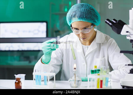 Portrait of young woman holding test tube over gas burner while working on scientific research in laboratory, copy space Stock Photo