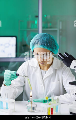 Portrait of young woman holding test tube over gas burner while working on scientific research in laboratory Stock Photo