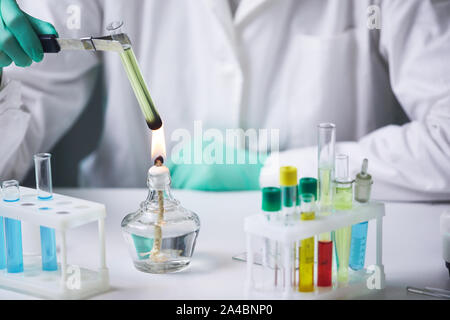 Close up of unrecognizable scientist holding test tube over gas burner while working on research experiment in laboratory, copy space Stock Photo