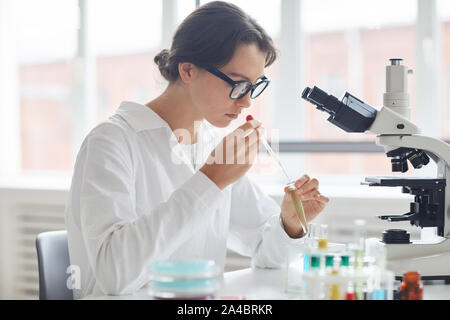 Side view portrait of beautiful young woman working in laboratory, preparing test samples for microscope research Stock Photo