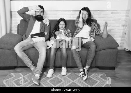 Tired parents and kid. Cleaning all day exhausting occupation. Exhausting cleaning day. Family mom dad and daughter with cleaning supplies sit on couch. Family care about cleanliness. Finish cleaning. Stock Photo