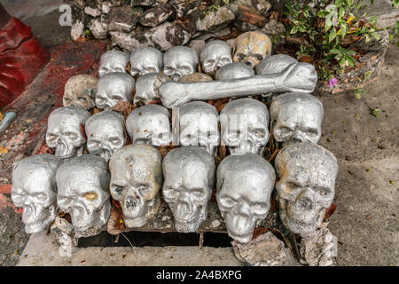 Bang Saen, Thailand - March 16, 2019: Garden of Hell in Wang Saensuk Buddhist Monastery. Closeup of pile of silver skulls and big bone in the dirt. Stock Photo