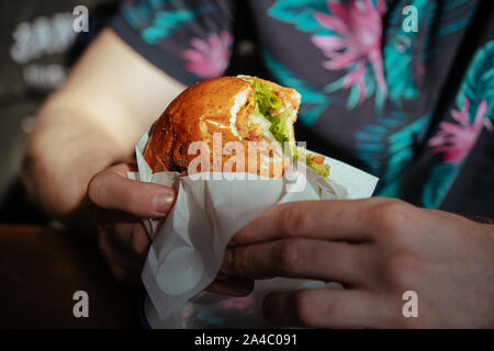 The guy holds a juicy hamburger in a summer cafe and lemonade on the table Stock Photo