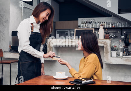 Young asian  barista is taking a credit card from customer at the cafe, customer paying coffee with credit card Stock Photo