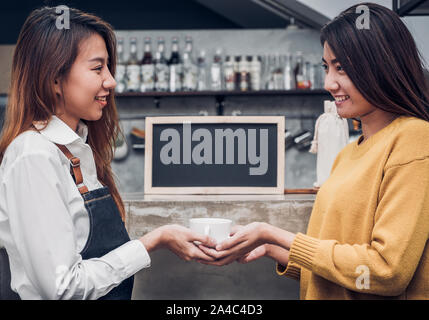 Young asian woman barista hold coffee cup serving a client at the coffee shop,start up small business owner food and drink concept. Stock Photo