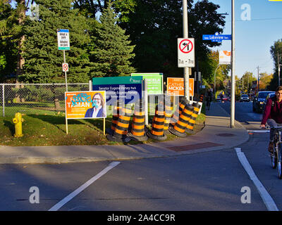 Orange bollards, a bus stop, cyclists and Federal election campaign posters make for a busy corner at Lakeview and Bronson, Ottawa, Ontario, Canada. Stock Photo