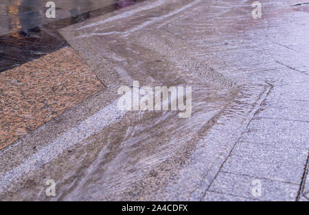 urban street gutter with water flow on tiled sidewalk at rainy day. background, weather. Stock Photo