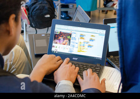 three students of color at a STEM high school using a laptop to code and program a game using a developer software Stock Photo
