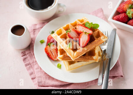 Square belgian waffles with strawberries served with cup of black coffee and chocolate sauce on pink background Stock Photo