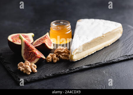 Brie or camembert cheese served with figs, honey and walnuts on black slate. Cheese plate Stock Photo