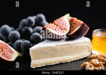Camembert or brie cheese slice with figs, black grapes, honey and walnuts on black background Stock Photo
