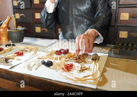 Traditional Chinese medicine practitioner talking on phone when packing dry roots and berries in paper Stock Photo