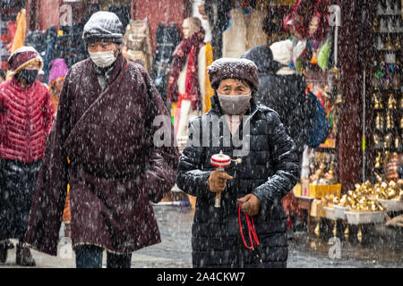 Lhasa, China - December 26 2018: Tibetan Buddhist woman performs a kora holding a prayer wheel around the  Jokhang temple in Lhasa old town in Tibet Stock Photo