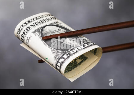 Chinese chopsticks hold one dollar, closeup. A concept on the relationship between America and China Stock Photo