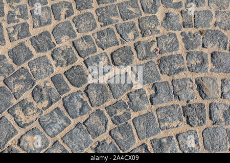 Cobbled road close-up. Abstract background of cobblestone pavement close-up. The pavement of stone. Brown texture of a paving stone track on a sand. Stock Photo