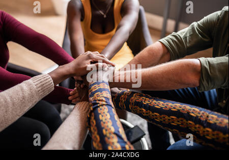 Cropped close of diverse businesspeople putting their hands on top of each other wearing casual clothes and african patterns. Stock Photo
