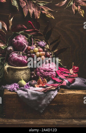 Still life with purple fruits and vegetables on wooden table with crockery, napkin and autumn leaves . Copy space for your design Stock Photo