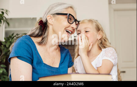 Cute preschool girl shares her sweet childish secrets with her joyful grandmother Stock Photo