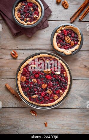 Autumn cranberries and pecan pies or tarts on wooden background, top view. Homemade seasonal pastry for Thanksgiving and autumn holidays. Stock Photo