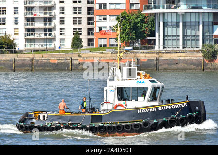 Close up side view of Haven Supporter tug & push bow boat with two crew members working on deck tugboat under way River Thames East London England UK