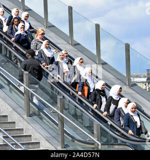 Group of school girls wearing Hijab headdress school uniform blazers & other people travel down outdoor escalator at Stratford England East London UK Stock Photo