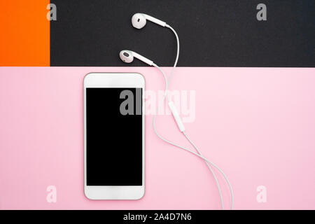 Music, gadgets, music lover. White smartphone and headphones on the orange, black and soft pink backgrounds with headphones. View from above. Flat lay Stock Photo