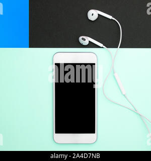 Music, gadgets, music lover. White smartphone and headphones on the blue, black and soft blue backgrounds with headphones. View from above. Flat lay, Stock Photo