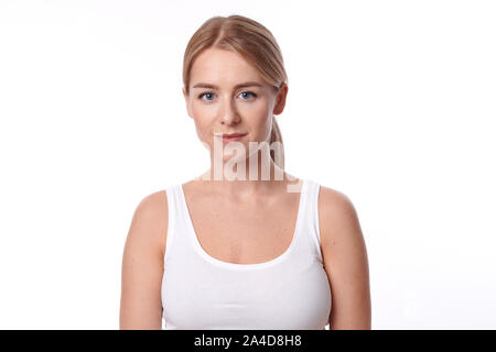 Attractive slender young woman in jeans and a white summer top standing looking intently at the camera with a quiet smile isolated on white Stock Photo