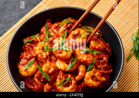 Schezwan Prawns in black bowl at dark slate background. Schezwan Prawns is indo-chinese cuisine curry dish with prawns or shrimps roasted in Schezwan Stock Photo