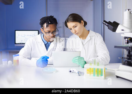 Team of young scientists using digital tablet while working on research in laboratory, copy space Stock Photo