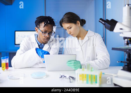 Two young scientists using digital tablet while working on research in laboratory, copy space Stock Photo