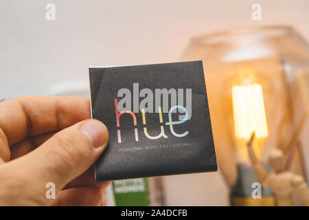 Paris, France - Sep 13, 2019: Man hand holding Philips Hue personal wireless lighting leaflet for the device with the filament led light turned on in the background Stock Photo